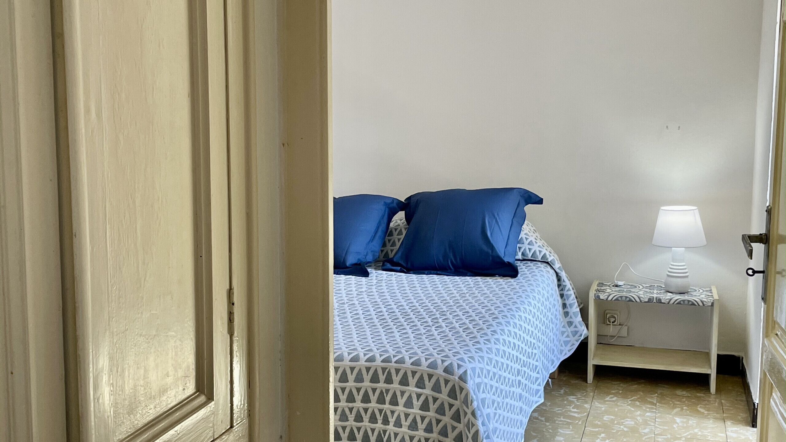 A bedroom with a bed, pillows, a nightstand, and a lamp.