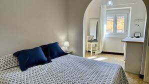 A bedroom with a bed, a nightstand, a chair, a desk, and a window.