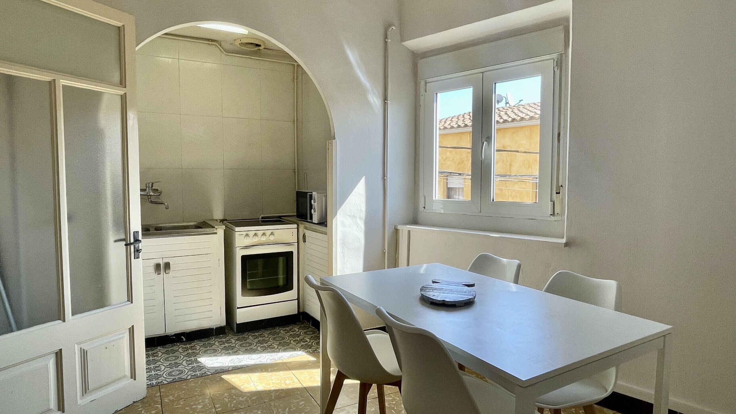 Una cocina compacta con estufa, horno y microondas. Hay una mesa de comedor con sillas y una ventana encima.