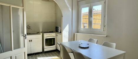 Una cocina compacta con estufa, horno y microondas. Hay una mesa de comedor con sillas y una ventana encima.