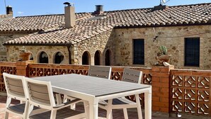 An outdoor patio with a table and chairs, a stone wall, and a tiled roof.