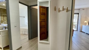 Ein Flur, der zu einem Schlafzimmer mit Holztür, einem Badezimmer mit Waschbecken und einer Balkonansicht führt.