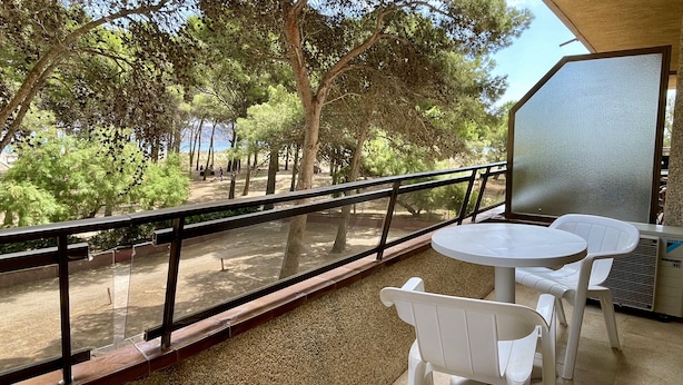 Ein Balkon mit Tisch und Stühlen, der einen Blick auf ein bewaldetes Gebiet mit Bäumen und das Meer bietet.