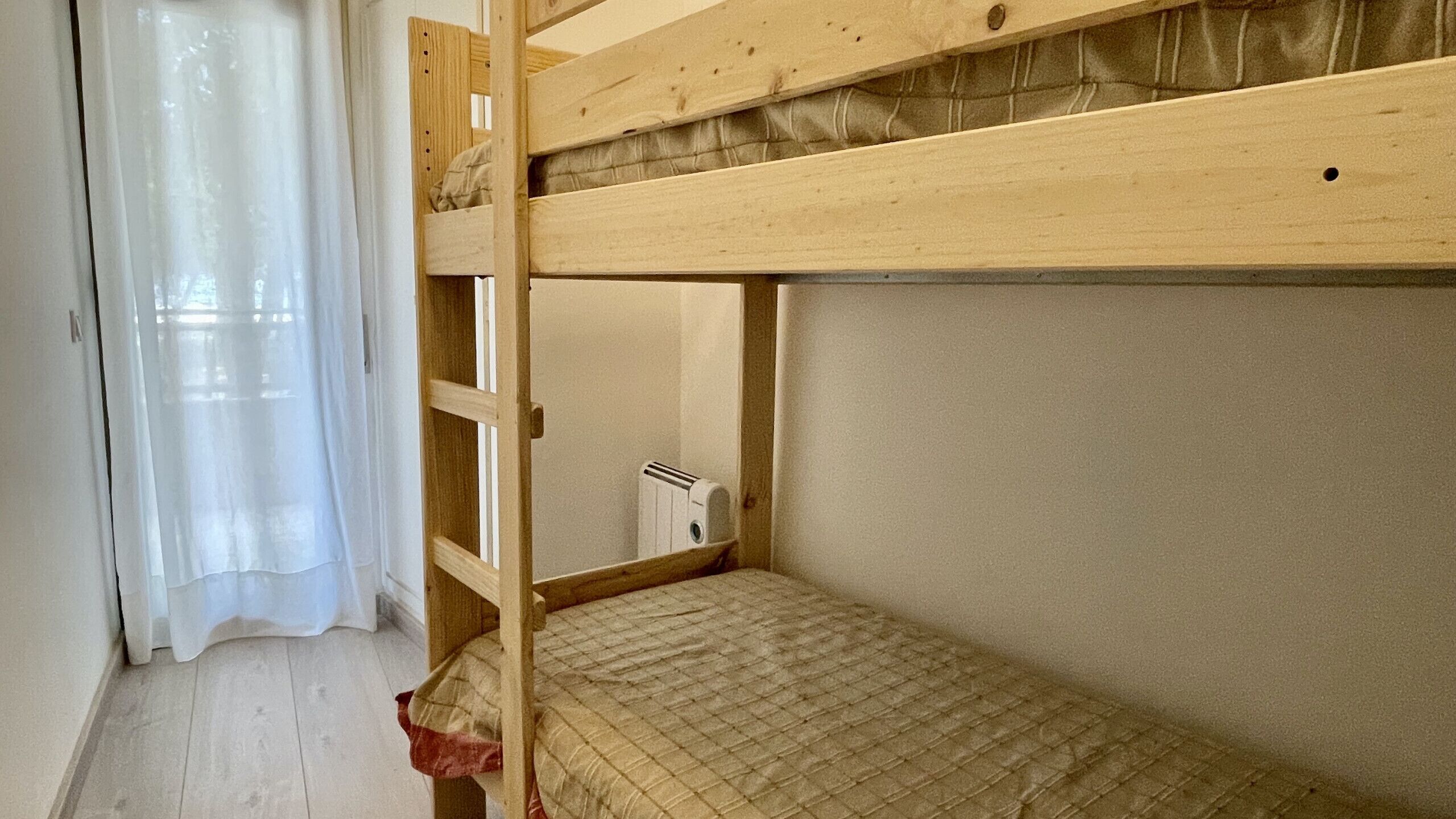 Dormitorio con literas, ventana, radiador y cortina.