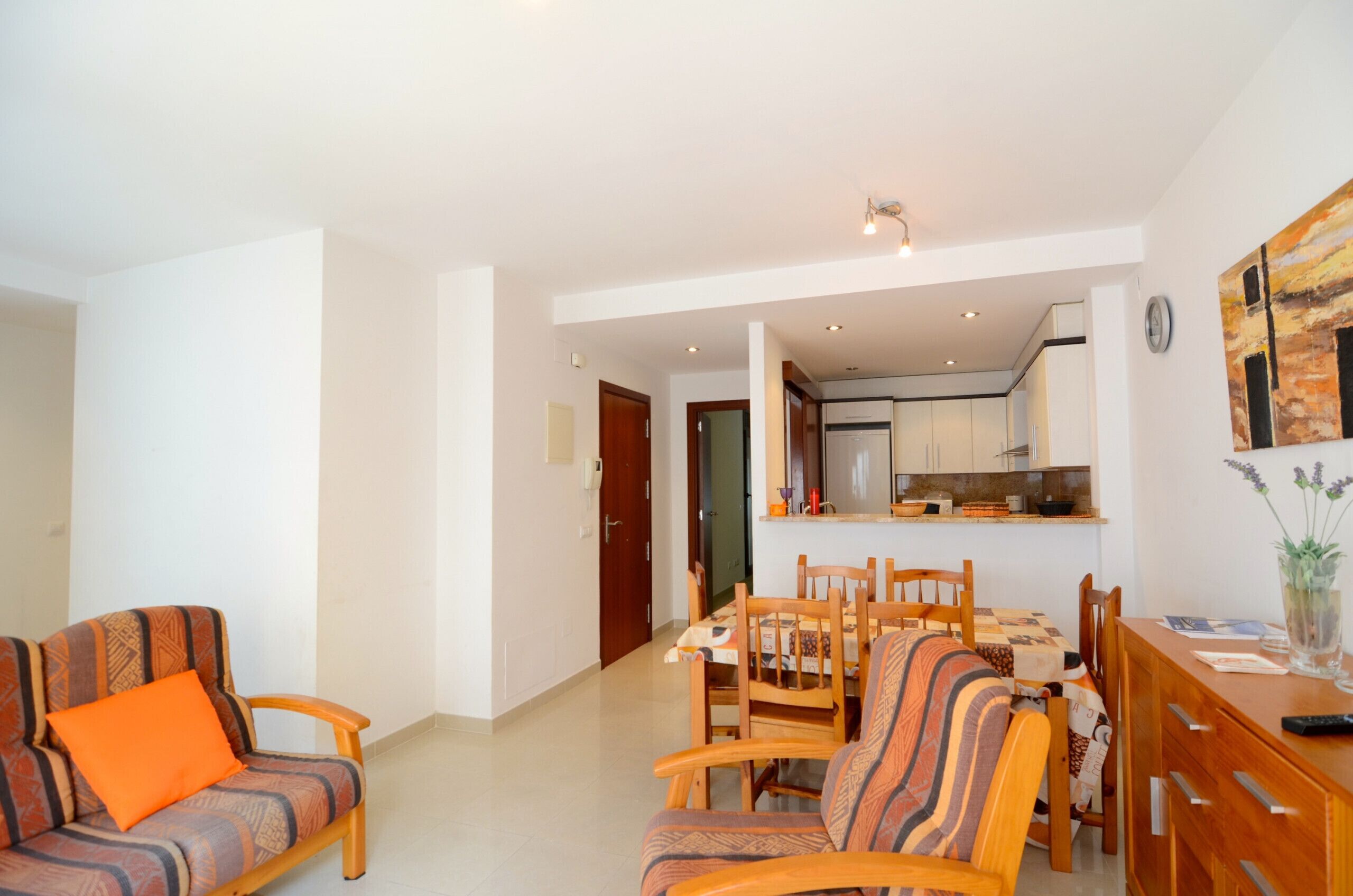 A modern living room with a sofa and chairs, a dining table, and a kitchen in the background.