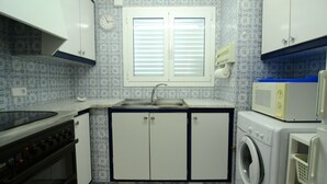 A compact kitchen with a sink, stove, microwave, and washing machine. - ENRIC SERRA 54 (L'Escala)