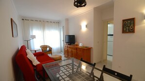 A compact living space with a red sofa, a glass dining table, a television, and a kitchen in the background. - ENRIC SERRA 54 (L'Escala)