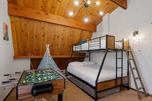 Une pièce avec un lit superposé, une table de baby-foot, un plafond en bois et un luminaire fixé au mur.