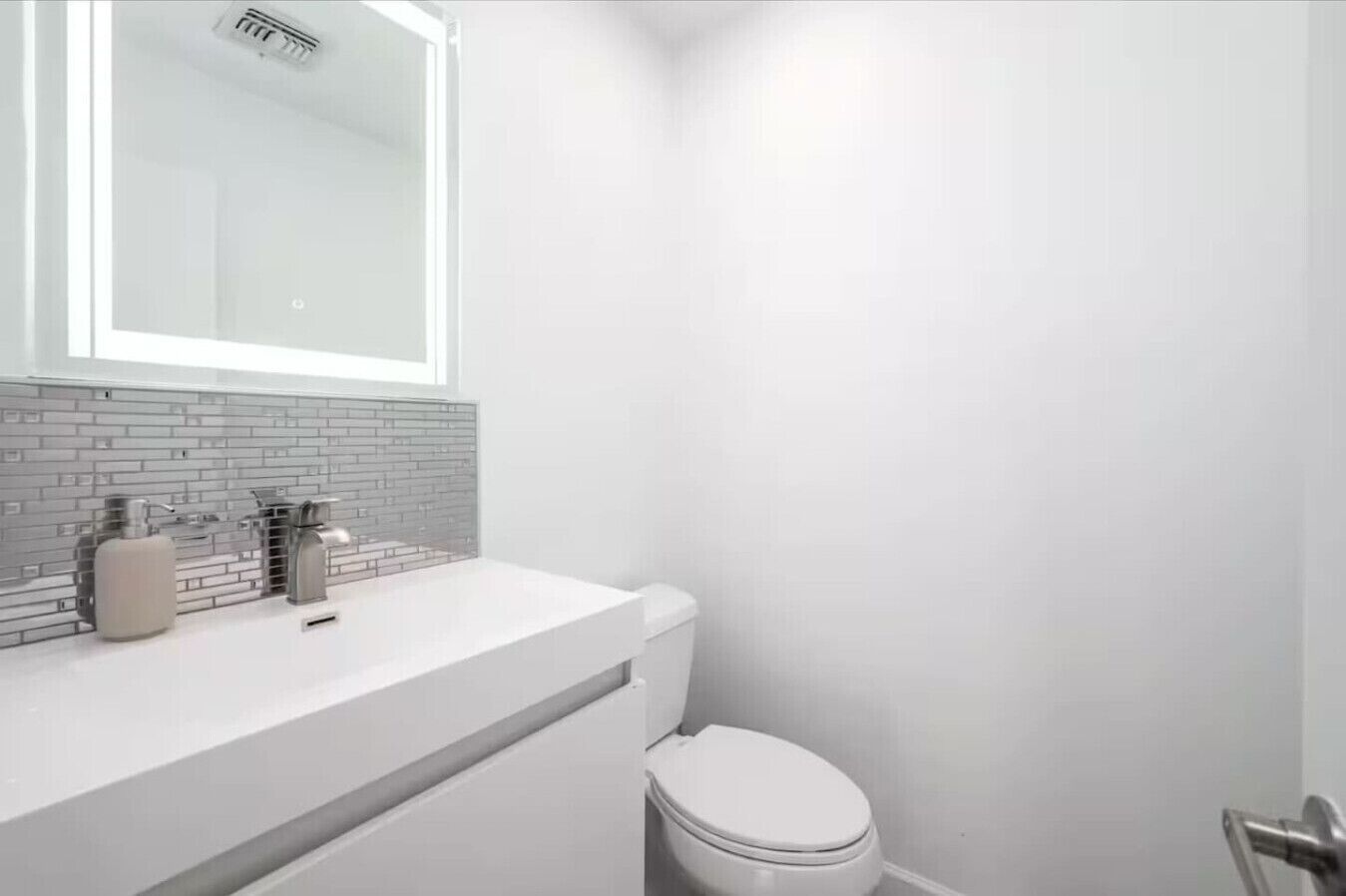 A bathroom with a white toilet, a sink with a mirror above it, and a tiled backsplash.