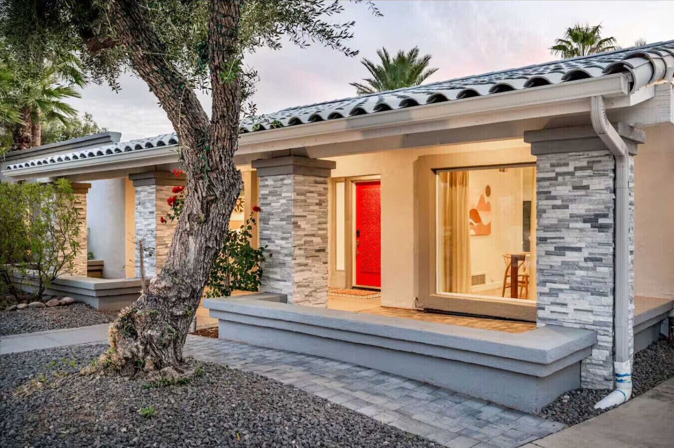 A modern house with a stone facade, a red door, and a large window.