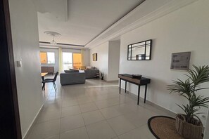 Ein modernes Wohnzimmer mit grauem Sofa, einem Couchtisch und einem Essbereich mit Tisch und Stühlen.