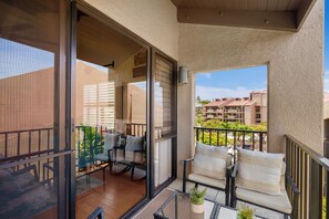 Un balcón con mobiliario exterior, una puerta de cristal que da a un espacio interior y vistas de edificios vecinos.