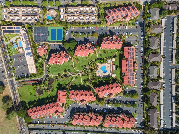 An aerial view of a residential area with multiple red-roofed buildings, a swimming pool, and a tennis court.