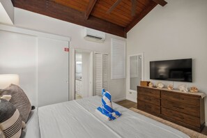 Una camera da letto con un letto, una TV, una cassettiera e un soffitto in legno.
