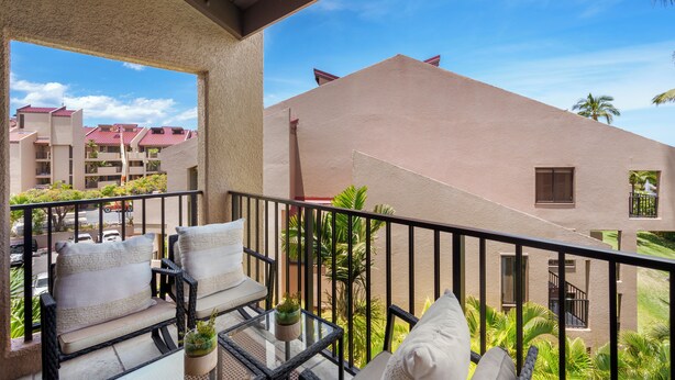 A balcony with outdoor furniture, a glass table, and a view of neighboring buildings.