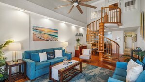 A spacious living room with a blue sofa, a coffee table, a wooden staircase, and a ceiling fan.