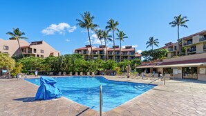 A swimming pool with lounge chairs and palm trees, surrounded by hotel buildings.