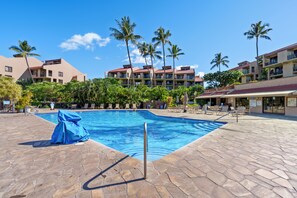 Una piscina con lettini e palme, circondata da edifici di un hotel.