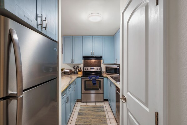 Una cocina estrecha con electrodomésticos de acero inoxidable, armarios azul claro y suelo de baldosas.