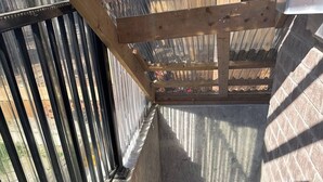 Una escalera de concreto con barandillas de metal que lleva a una zona cubierta con techo de láminas corrugadas.