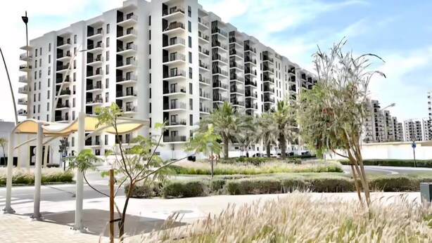 Een modern meerlaags woongebouw met balkons, omringd door aangelegde groene zones en palmbomen.