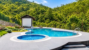 Una piscina con un pequeño edificio, rodeada de vegetación exuberante y un paisaje montañoso.