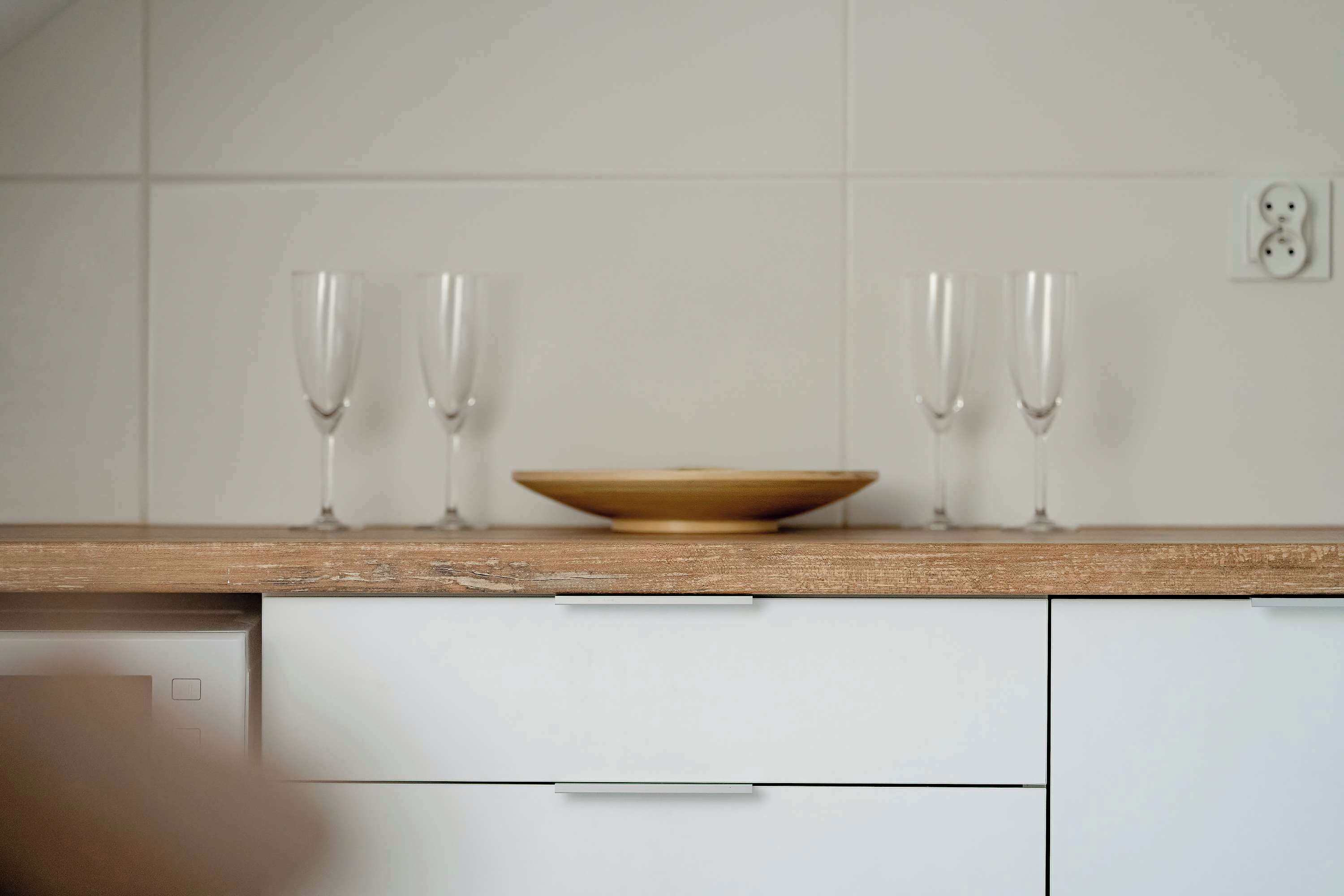 A kitchen with a wooden countertop, two white cabinets, and a white wall with a power outlet.