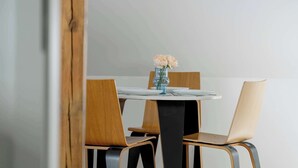 A dining area with a round table, two wooden chairs, and a vase with flowers.