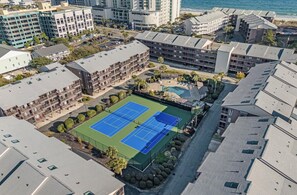 Vista aérea de un complejo hotelero con varias edificaciones, una cancha de tenis y una zona de piscina.