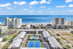 Un hotel de gran altura con piscina y canchas de tenis, con vistas a una playa y al océano.