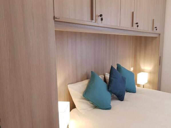 Ein Schlafzimmer mit einem Bett, Kissen in Türkis und Weiß sowie einem Nachttisch mit einer Lampe.
