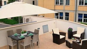 An outdoor patio with a dining table set for four, surrounded by wicker chairs, a large umbrella, and a sofa. - L&G's Roof Terrace, near the Tower of Pisa. (Pisa)