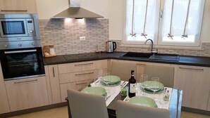 A modern kitchen with a built-in oven, microwave, and stainless steel range hood. There is a dining table set with green plates and wine glasses, and a bottle of wine on the table. - L&G's Roof Terrace, near the Tower of Pisa. (Pisa)