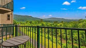 A balcony with a table and chairs, overlooking a lush green landscape with mountains in the distance. - Mountain Views Indoor Pool & Sauna Fireplace (Gatlinburg)