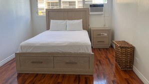 Un dormitorio con una cama de madera, una mesita de noche, una cesta de mimbre y una ventana con persianas.