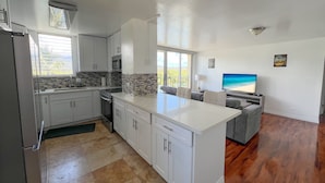 Una cocina moderna con armarios blancos, una isla grande y un comedor con vista al océano.