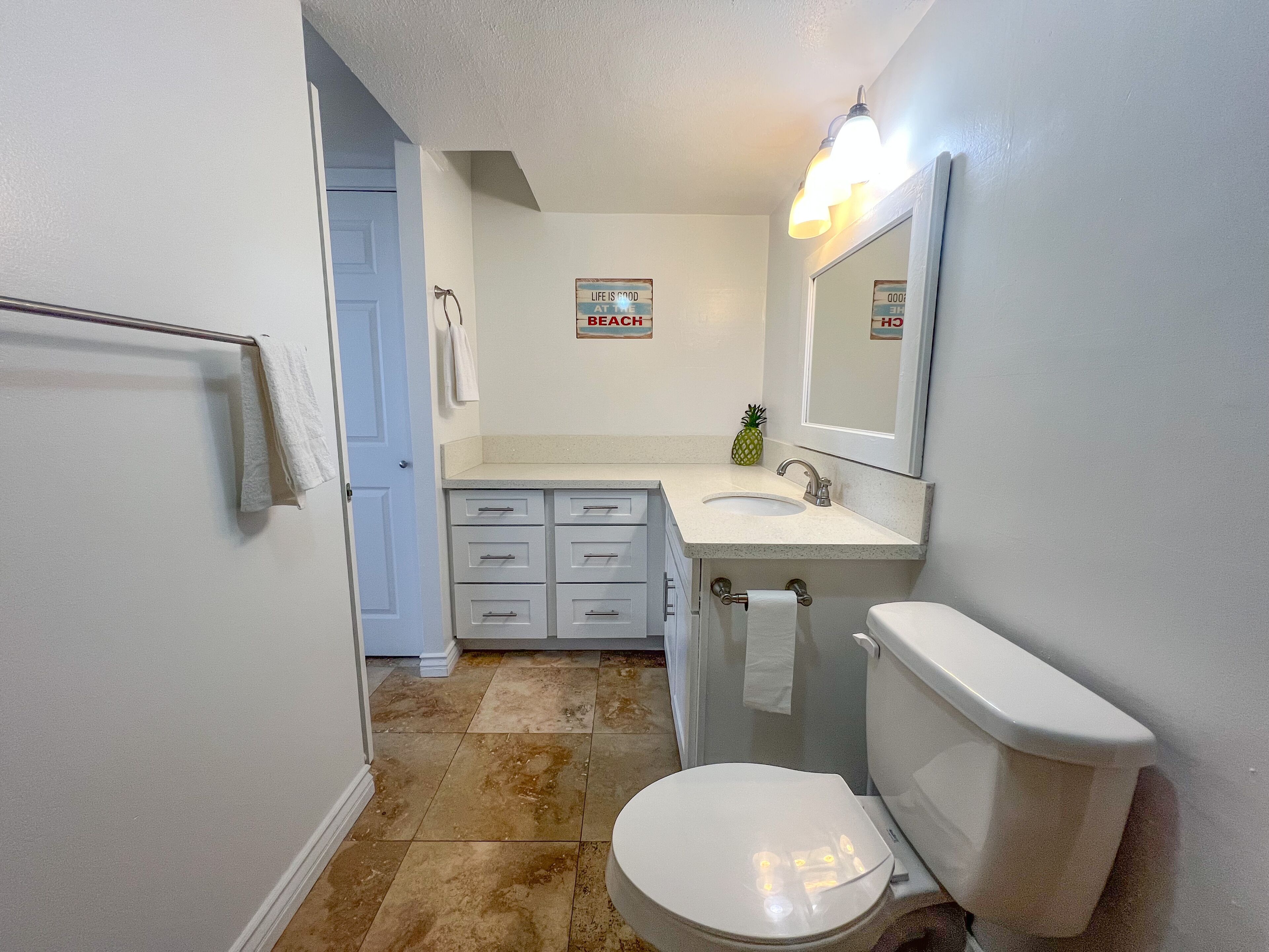 A bathroom with a toilet, sink, and vanity with drawers. There is a towel rack and a sign on the wall.