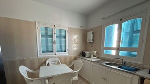 Une petite cuisine avec une table et des chaises blanches, un four à micro-ondes, un grille-pain et un évier.