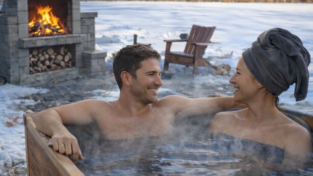 A wooden hot tub with a stone fireplace in the background.