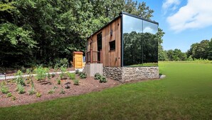 A modern wooden structure with a glass extension, surrounded by a well-maintained garden and trees.