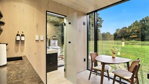 A modern bathroom with a glass shower enclosure, wooden walls, and a view of a well-maintained garden through large windows.