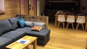 A modern living room with a dark grey sofa, a wooden coffee table, and a dining area with white chairs.