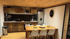 A modern kitchen with wooden cabinets, a stainless steel refrigerator, a microwave, and a dining area with a wooden table and white chairs.