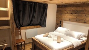 A wooden bunk bed with a window, a wooden chair, and a bedside table.