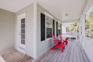 Une véranda couverte avec une balustrade blanche, un plancher en bois et des fauteuils Adirondack rouges.