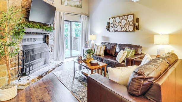 A living room with a stone fireplace, leather sofa, and a flat-screen TV mounted on the wall. - Ski, Hike & Explore: Mtn-view Haven in Gatlinburg! (Gatlinburg)