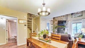 A dining area with a wooden table, chairs, and a chandelier. There is a staircase leading to another level and a living room with a fireplace and a television. - Ski, Hike & Explore: Mtn-view Haven in Gatlinburg! (Gatlinburg)