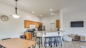 A modern kitchen with wooden cabinets, a central island with stools, a microwave, and a refrigerator. - 3 Mi to London Bridge Beach - 'ggs River Retreat' (Lake Havasu City)