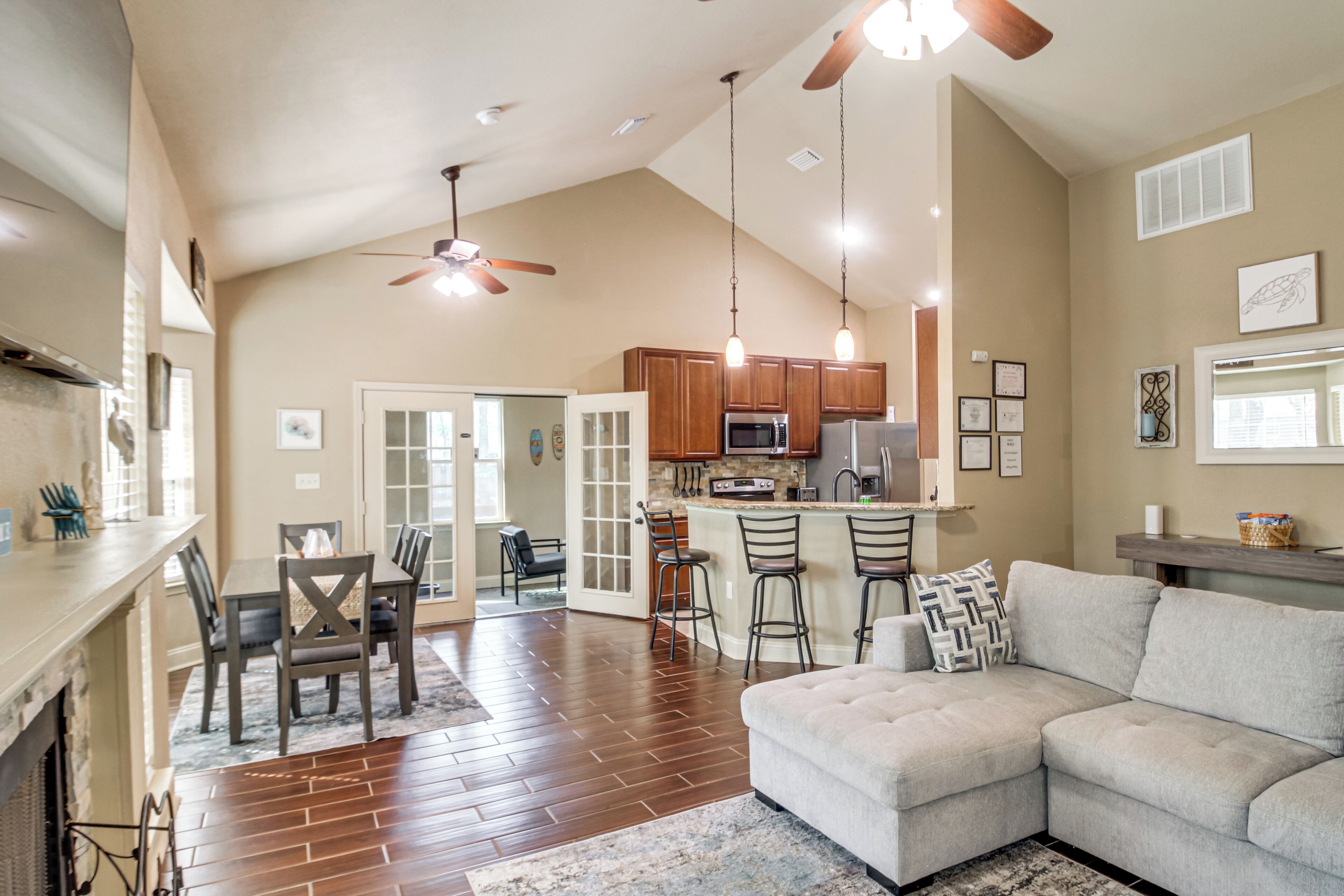 A spacious living area with a large sectional sofa, a dining table with chairs, a kitchen with wooden cabinets, and a ceiling fan.