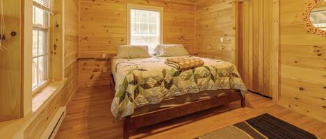 Un dormitorio de cabaña de madera con una cama, un ventilador de techo, una ventana y una puerta.